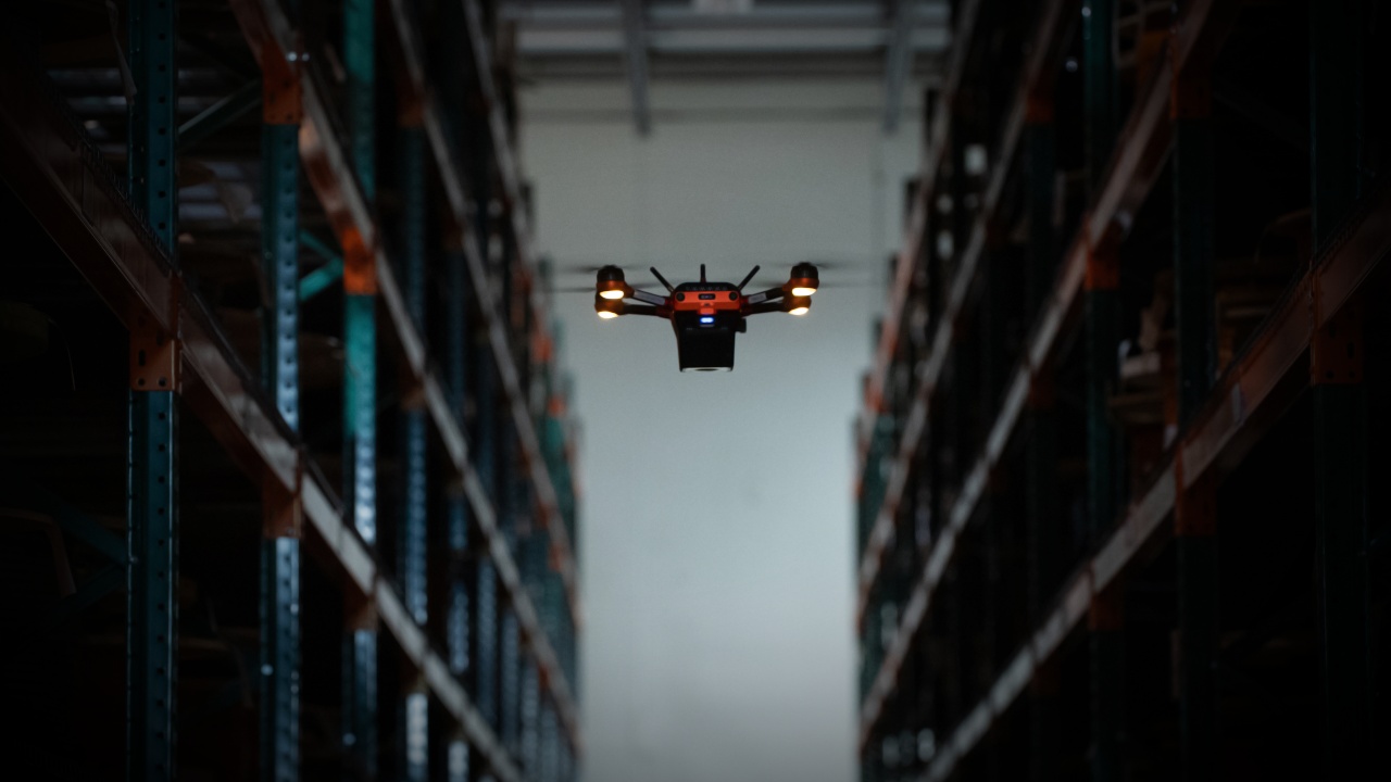 A Corvus One warehouse drone flies through a dark aisle as it scans inventory.