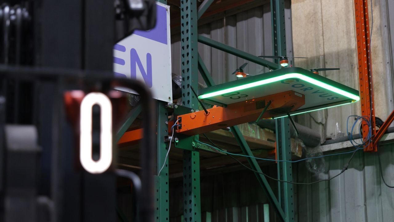 Corvus Trident attached to a reach truck in the foreground with a Corvus One autonomous inventory drone sitting on it's landing pad mounted to a rack in the background.